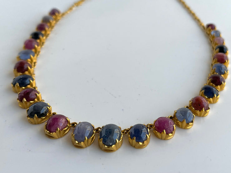 A tightly focused shot showcases the smooth, polished surfaces of the cabochon-cut sapphires and rubies. Each stone is securely bezel-set with prongs, emphasizing the handcrafted quality and allowing the deep blues and vibrant reds to shine against the golden setting.