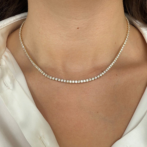 Close-up of a yellow gold diamond tennis necklace on a model wearing a white blouse.