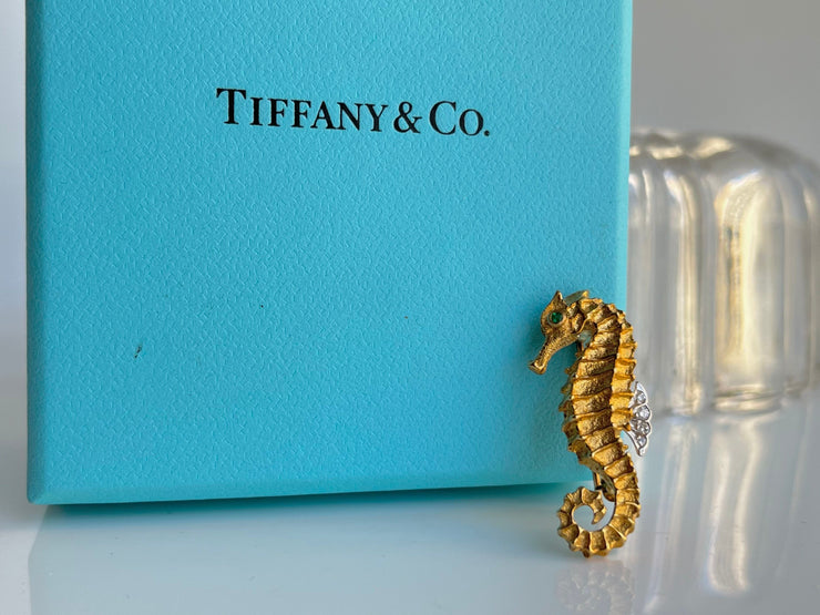 The brooch is elegantly presented next to an Iconic blue Tiffany and Co box, enhancing its golden hue and luxurious accents.