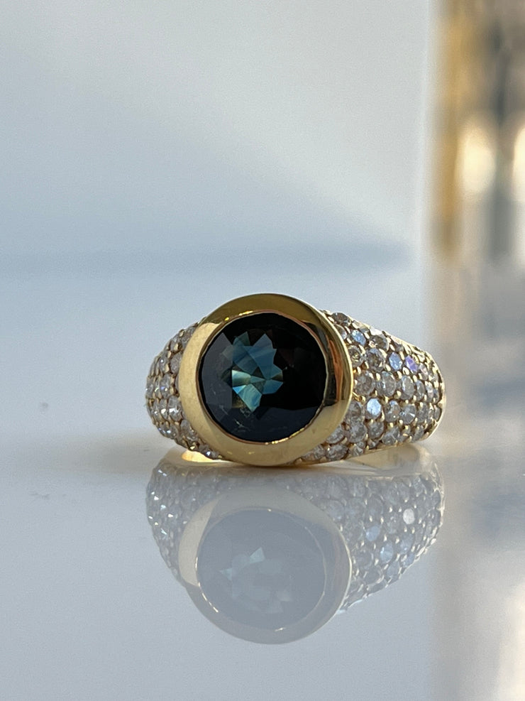 An elegant view of the ring showcasing the vivid 2.60 carat round-cut natural blue sapphire at the center, framed by sparkling round brilliant diamonds. The polished 14K yellow gold setting adds warmth and contrast to the gemstone's rich hue.
