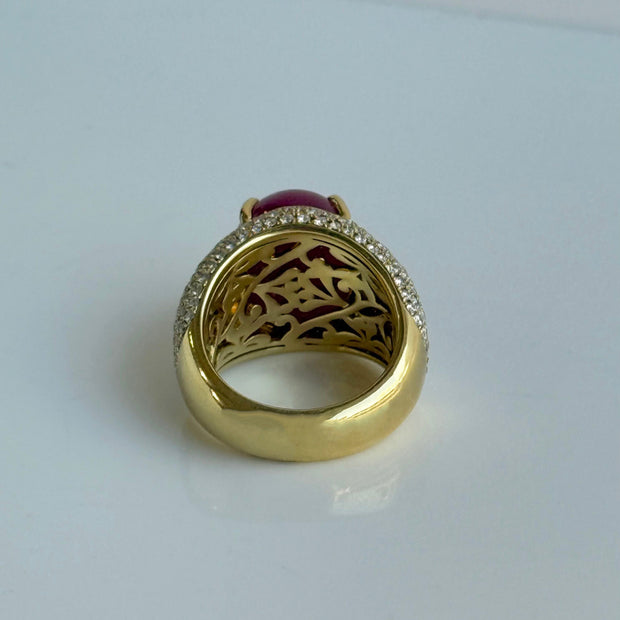 Gold ring with a red ruby cabochon gemstone and diamond accents on a light gray background