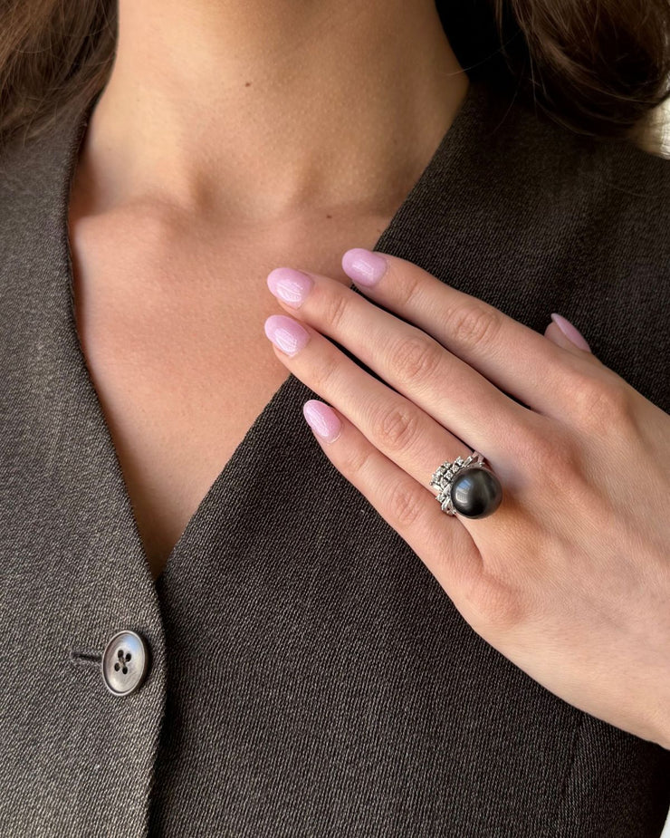 Close-up of a hand wearing a diamond  black pearl ring with a brown blazer background