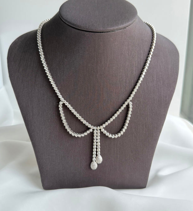 Diamond bow tennis necklace on a mannequin bust with a white background