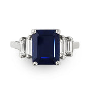 Ring with a blue sapphire gemstone and natural diamond baguette side stones on a white background