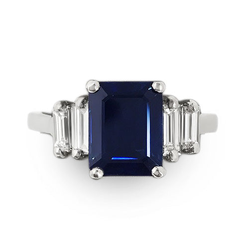 Ring with a blue sapphire gemstone and natural diamond baguette side stones on a white background