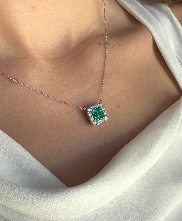 Close-up of a model wearing an 18k white gold necklace adorned with a 1.51 ct light green emerald and a sparkling diamond halo, highlighted by two accent diamonds along the chain.