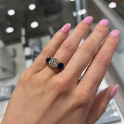 Hand wearing a ring with a diamond and sapphires in a jewelry store setting