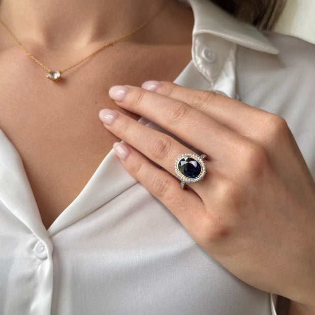 Close-up of a hand wearing a deep blue sapphire gemstone ring with a white silk shirt background