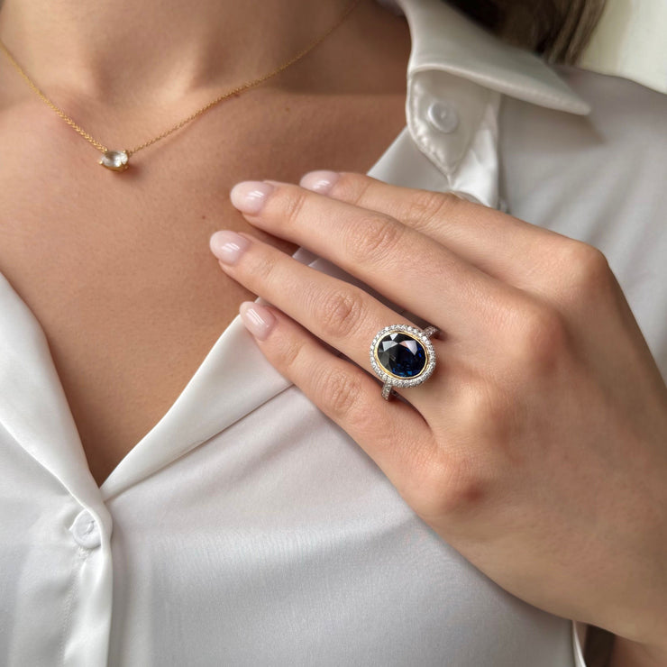 Close-up of a hand wearing a deep blue sapphire gemstone ring with a white silk shirt background