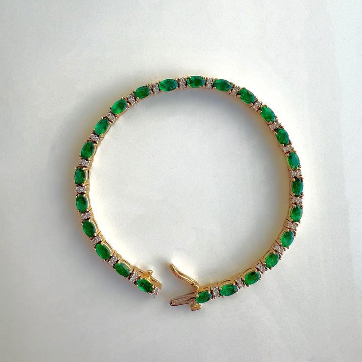 The bracelet displayed against a clean background, highlighting the vibrant green emeralds and shimmering diamonds in a luxurious 14k yellow gold setting.