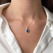 Necklace with a blue sapphire gemstone pendant worn by a model in a silk white shirt.
