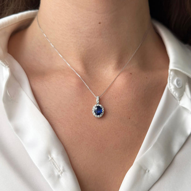 Necklace with a blue sapphire gemstone pendant worn by a model in a silk white shirt.