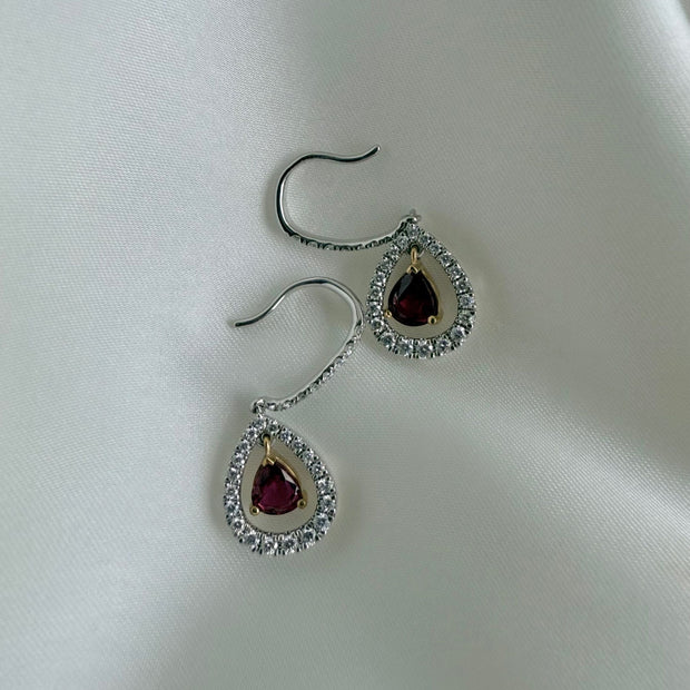 Luxury ruby drop earrings featuring contrasting yellow prongs against white gold on silk background