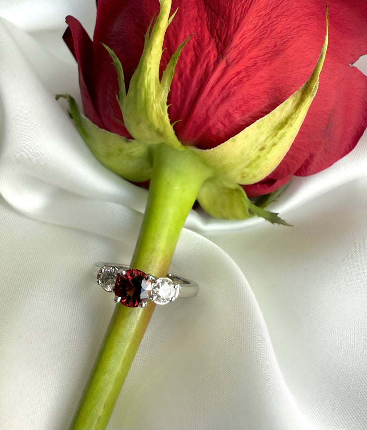 Beautiful red spinel estate and diamond three stone ring with a silk background placed next to a rose. 