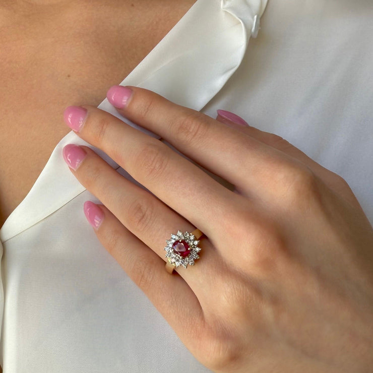 Hand wearing a ring with a red ruby gemstone against a white shirt background