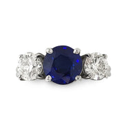 An 18k white gold ring featuring a round faceted blue sapphire center stone flanked by two round brilliant diamonds.