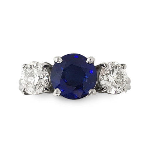 An 18k white gold ring featuring a round faceted blue sapphire center stone flanked by two round brilliant diamonds.