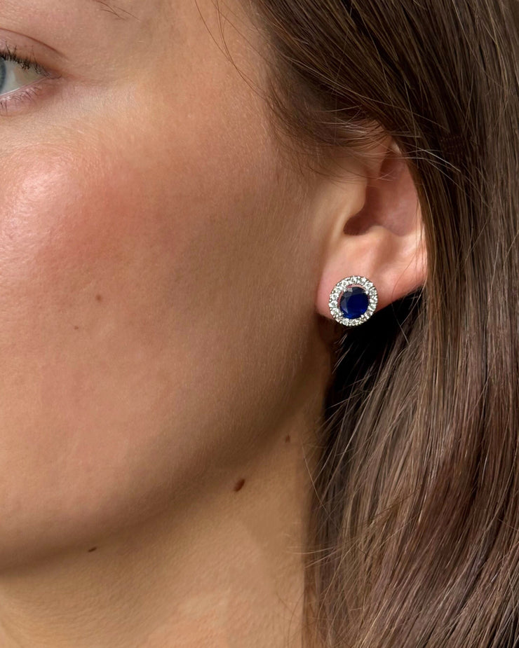 Close-up of a person wearing blue sapphire gemstone earrings with a white gold setting.