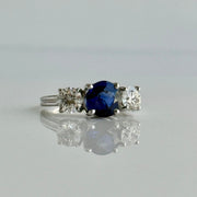Stunning deep blue sapphire flanked by two round brilliant natural diamonds on a ring set in 18k white gold