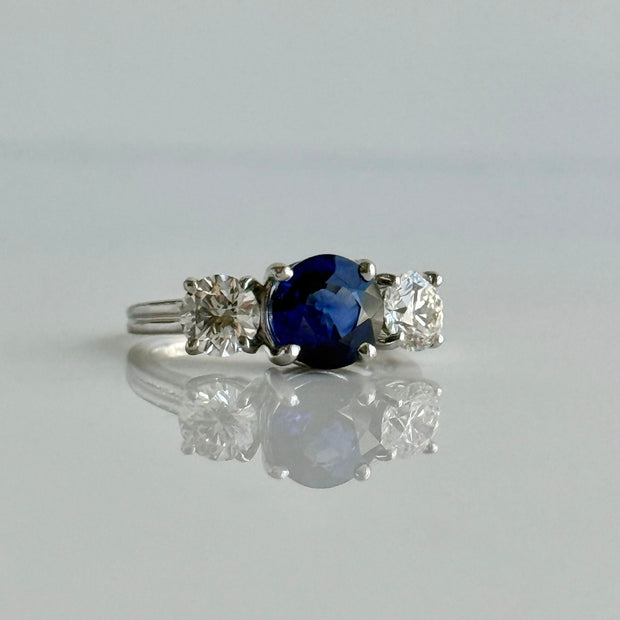 Stunning deep blue sapphire flanked by two round brilliant natural diamonds on a ring set in 18k white gold