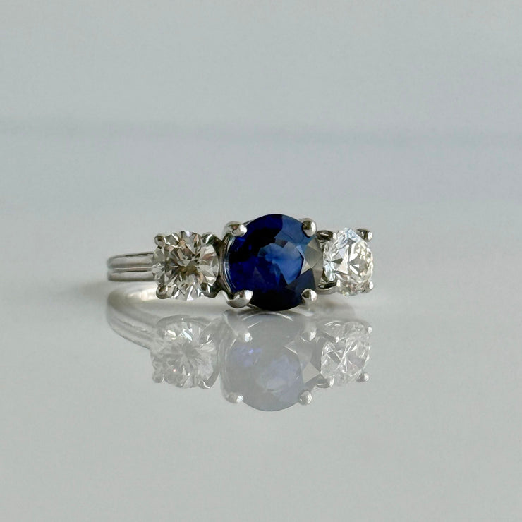 Stunning deep blue sapphire flanked by two round brilliant natural diamonds on a ring set in 18k white gold