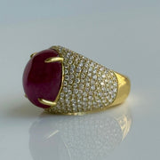 Side angle of red ruby cabochon ring with diamond-studded band on a light gray background