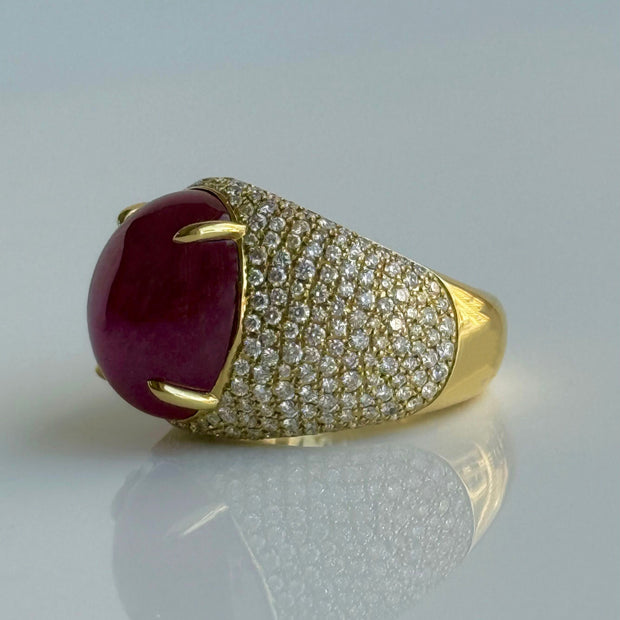 Side angle of red ruby cabochon ring with diamond-studded band on a light gray background