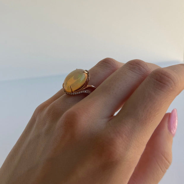 Hand wearing a rose gold ring with a large opal gemstone on a white background