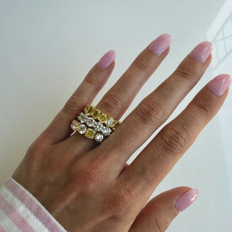 Hand wearing three white and yellow diamond eternity rings stacked on a white background