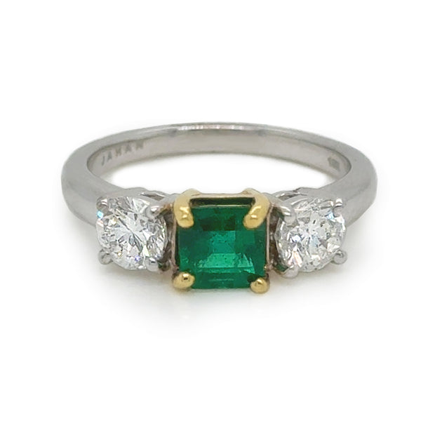 Emerald at the center set in yellow gold, flanked by two round brilliant cut side diamonds set in white gold.