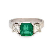 Ring with a green emerald gemstone and two smaller diamonds on a white background