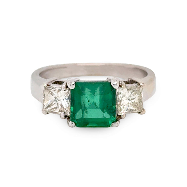 Ring with a green emerald gemstone and two smaller diamonds on a white background