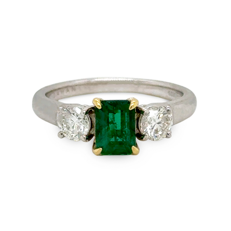 Ring with a green emerald gemstone and two smaller diamonds on a white background