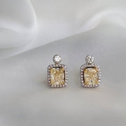 Pair of yellow diamond stud earrings on a white fabric background