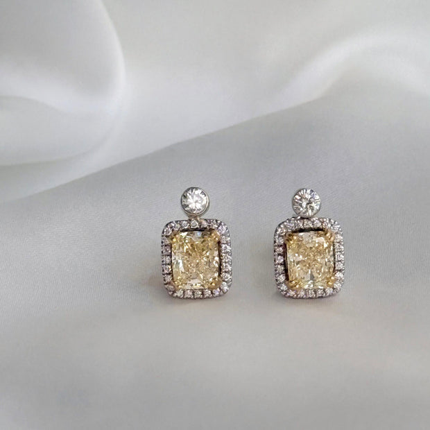 Pair of yellow diamond stud earrings on a white fabric background