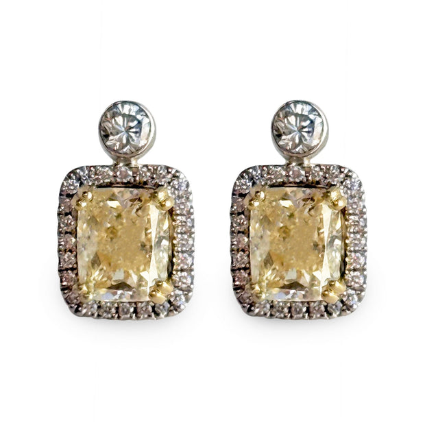 Pair of earrings with large yellow diamonds and smaller white diamond halo on a white background