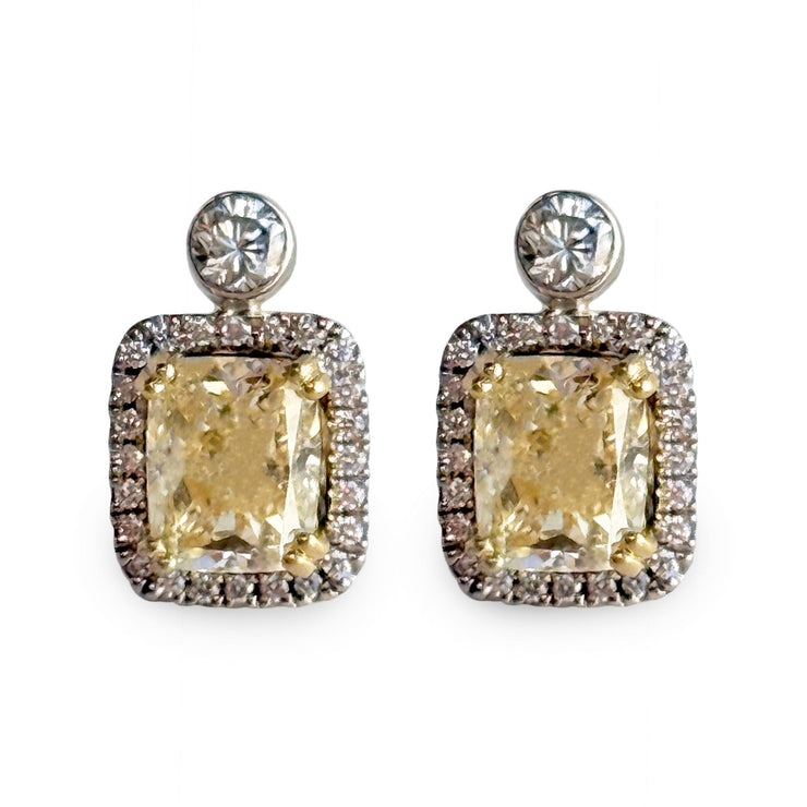 Pair of earrings with large yellow diamonds and smaller white diamond halo on a white background