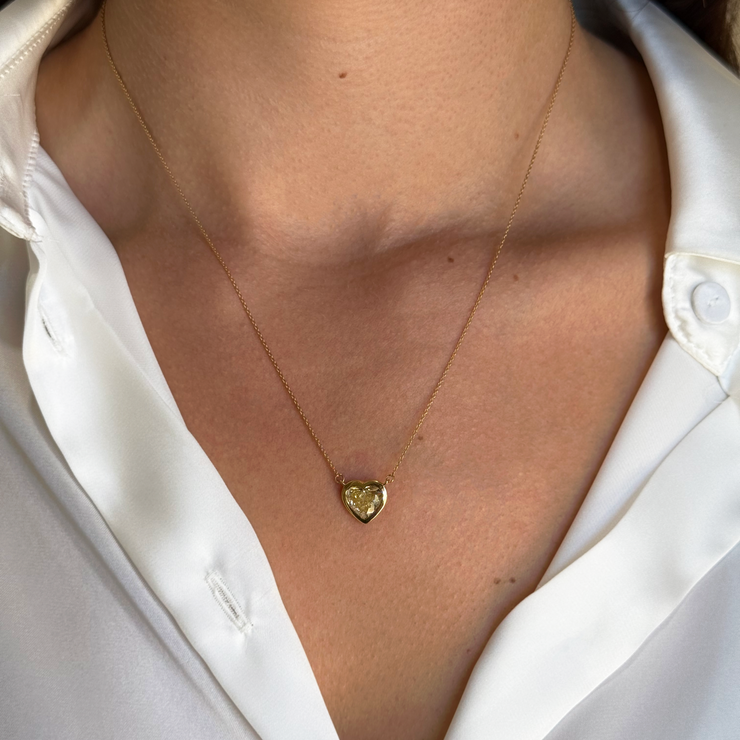 Gold heart-shaped yellow diamond necklace worn by a model in a white shirt.