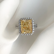 Ring with a large yellow diamond and smaller diamond halo on a white background