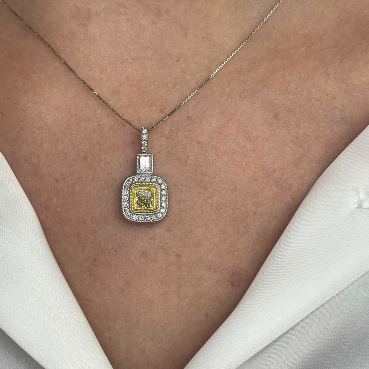 White and yellow gold necklace with a fancy yellow cushion-cut diamond pendant and a halo set of round brilliant and emerald cut diamonds.