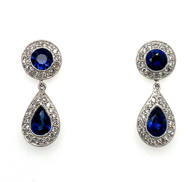 A pair of dangle earrings featuring sapphire gemstones with diamond halos, set in a platinum band.