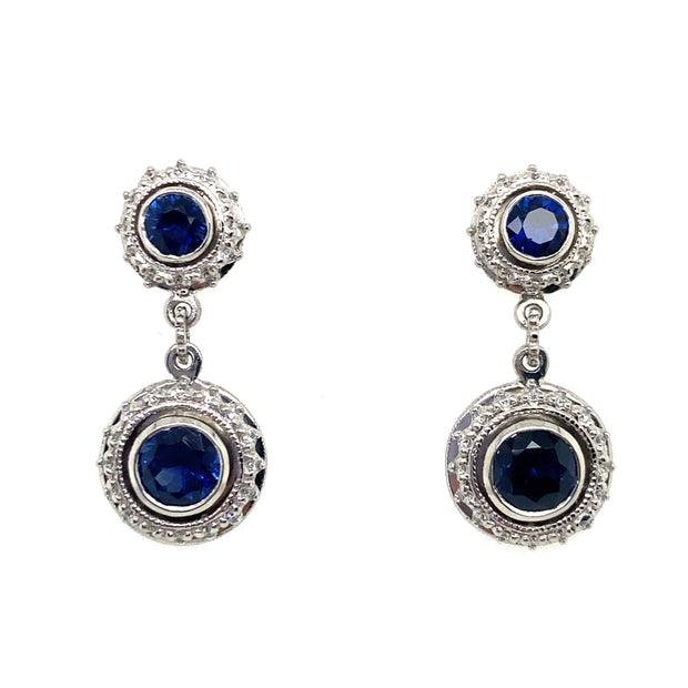 A pair of dop earrings with blue sapphire centers with diamond halos, set in platinum.