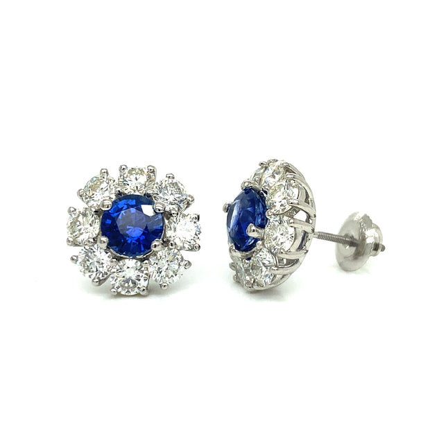 A pair of platinum stud earrings featuring a central sapphire with round brilliant diamond halos.