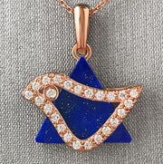 A rose gold dove pendant set with round brilliant cut diamonds, mounted on a lapis lazuli background.