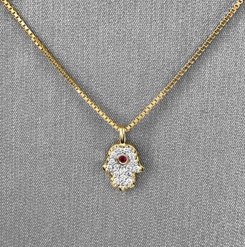An 18 Karat Yellow Gold petite Hamsa pendant with pave-set round brilliant cut diamonds and a bezel-set ruby at the center, attached to a 14 Karat Yellow Gold chain.