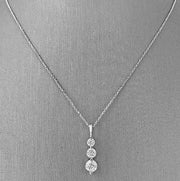 A 14 karat white gold three diamond pendant necklace with round brilliant cut diamonds.