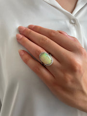 A model wearing a large 5.80-carat cabochon cut oval opal ring, reflecting stunning colors in the light, showcasing its vibrant beauty.