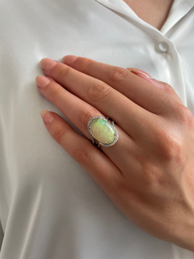 A model wearing a large 5.80-carat cabochon cut oval opal ring, reflecting stunning colors in the light, showcasing its vibrant beauty.