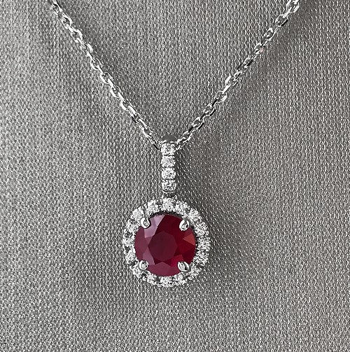 0.80 carat vivid round ruby center stone with 0.11 carats total weight of round brilliant cut diamonds on the halo and bail.