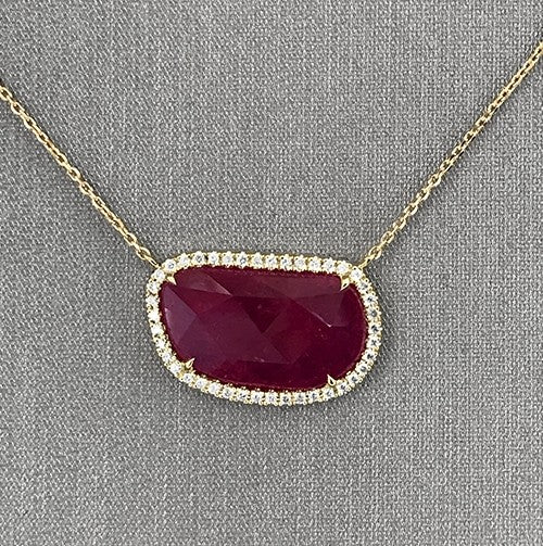 Closer detailing the faceted ruby slice with round brilliant  diamond halo.